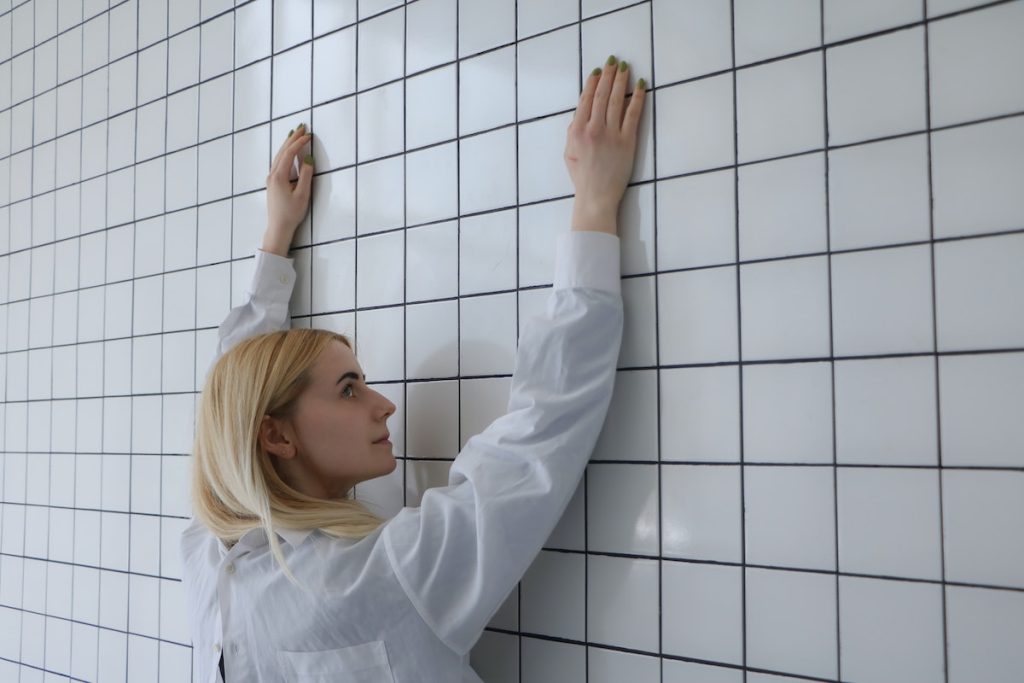 Blond woman with raised arms near tiled wall